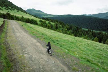 Çiçekli çayır dağ patikasında dağ bisikleti süren kadının hava manzarası.