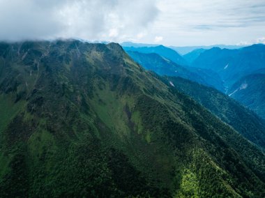 Bulutlu gökyüzünün altında yemyeşil dağlar