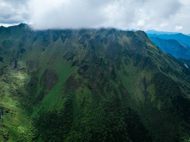 Bulutlu gökyüzünün altında yemyeşil dağlar