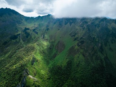 Bulutlu gökyüzünün altında yemyeşil dağlar