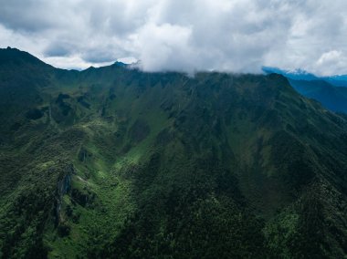 Bulutlu gökyüzünün altında yemyeşil dağlar