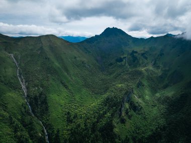 Bulutlu gökyüzünün altında yemyeşil dağlar