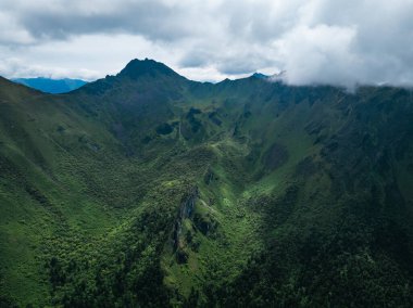 Bulutlu gökyüzünün altında yemyeşil dağlar
