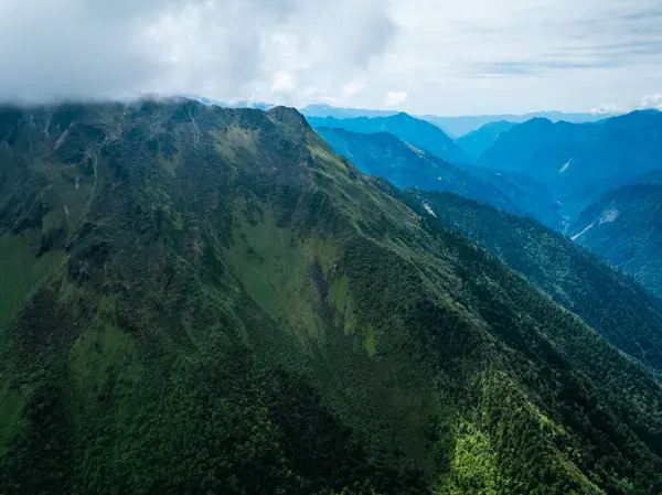Bulutlu gökyüzünün altında yemyeşil dağlar