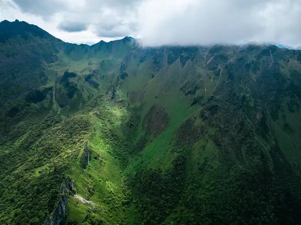 Bulutlu gökyüzünün altında yemyeşil dağlar