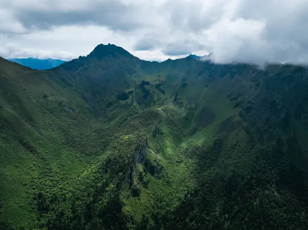 Bulutlu gökyüzünün altında yemyeşil dağlar