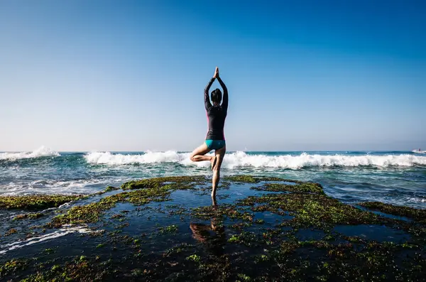 Kadın, yaklaşan güçlü deniz dalgalarıyla yüzleşmek için deniz kenarındaki uçurumun kenarında yoga yapıyor.