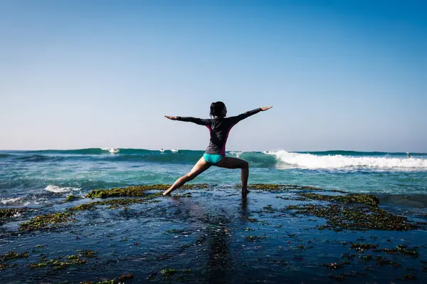 Kadın, yaklaşan güçlü deniz dalgalarıyla yüzleşmek için deniz kenarındaki uçurumun kenarında yoga yapıyor.