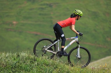 Dağın tepesinde dağ bisikleti süren Asyalı bir kadın.