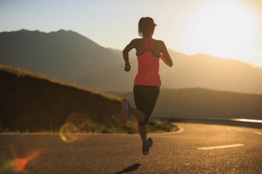 Gün batımında dağ yolunda koşan kadın koşucu 