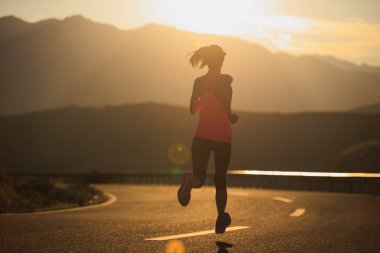 Gün batımında dağ yolunda koşan kadın koşucu 