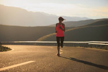 Gün batımında dağ yolunda koşan kadın koşucu 