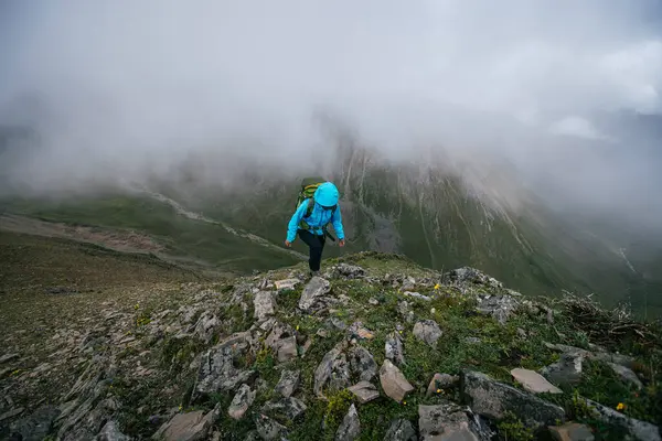 Tibet 'te dağın tepesine tırmanan bir kadın yürüyüşçü 