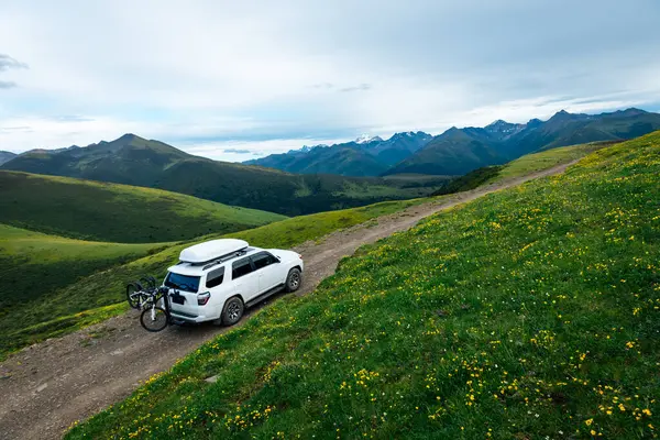 Offroad arabası mavi gökyüzünün altında çiçek açan çayır dağında bisiklet taşıyor.