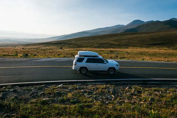 Araba güneşin doğuşunda yüksek irtifada dağın tepesinde ilerliyor.