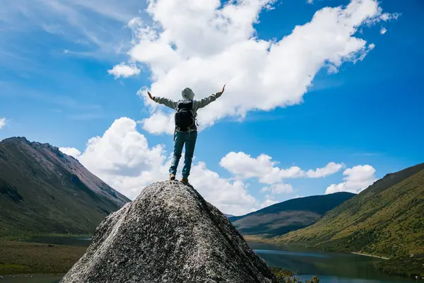 Sırt çantalı bir kadın yüksek irtifada dağ tepesinde yürüyüş yapıyor. Uzakta bir göl var.