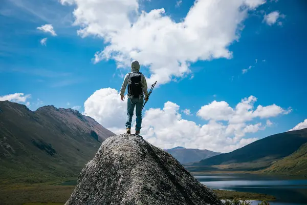 Yüksek irtifada dağ tepesinde yürüyüş yapan bir kadın. Uzakta bir göl.