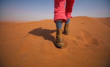 Çölde yürüyen deri çizme giyen bir kadın.