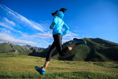 Patika koşucusu yüksek irtifada çayırların tepesindeki yolda koşuyor.