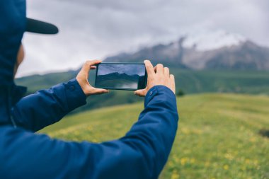 Otlağın tepesinde akıllı telefonla fotoğraf çeken bir kadın yürüyüşçü.