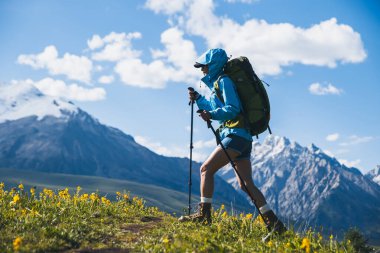 Sırt çantalı bir kadın otlakta yürüyüş yapıyor.