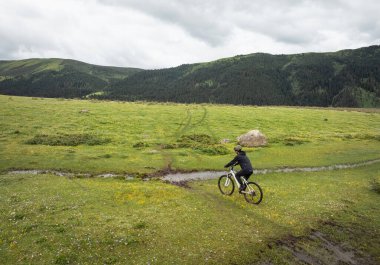 Çiçekli çayır dağ patikasında dağ bisikleti süren kadının hava manzarası.