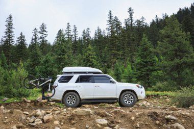 Offroad arabası mavi gökyüzünün altında çiçek açan çayır dağında bisiklet taşıyor.