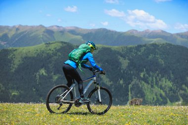 Uçsuz bucaksız gökyüzünün altındaki engebeli dağlara bakan yeşil bir yamaçta bisiklet pedalları.