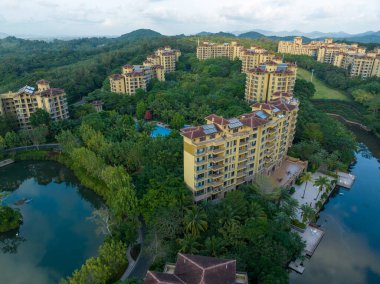 Huzurlu bir göle bakan, yemyeşil bir ormanın içine yerleştirilmiş modern tatil köyü apartmanları. Hainan ili, Çin. 