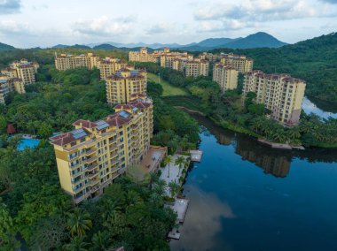 Hainan Bölgesi, Çin. Huzurlu bir göle bakan, yemyeşil bir ormanın içine kurulmuş modern tatil köyü binaları.