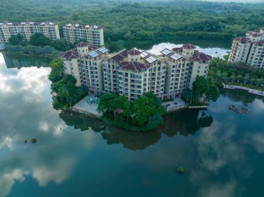 Huzurlu bir göle bakan, yemyeşil bir ormanın içine yerleştirilmiş modern tatil köyü apartmanları. Hainan ili, Çin. 