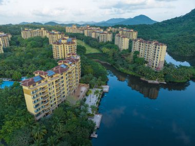 Huzurlu bir göle bakan, yemyeşil bir ormanın içine yerleştirilmiş modern tatil köyü apartmanları. Hainan ili, Çin. 