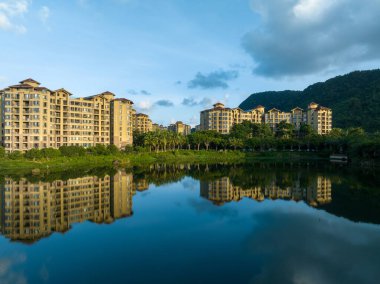 Hainan Bölgesi, Çin. Huzurlu bir göle bakan, yemyeşil bir ormanın içine kurulmuş modern tatil köyü binaları.
