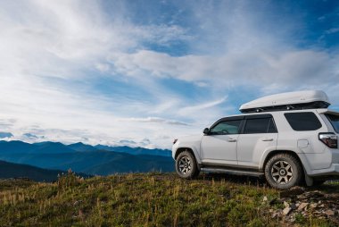 Araba dağlara ve mavi gökyüzüne park edilmiş.