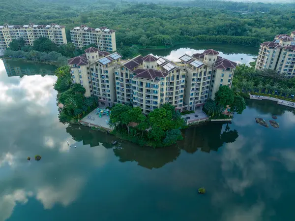 Huzurlu bir göle bakan, yemyeşil bir ormanın içine yerleştirilmiş modern tatil köyü apartmanları. Hainan ili, Çin. 