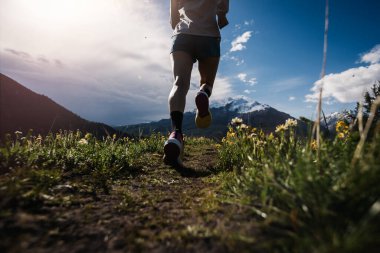 Dağlarda koşarken spor ayakkabılar ve spor giysiler giyen birinin kırpılmış görüntüsü.  