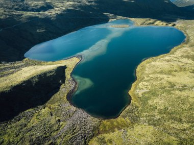 Aerial view of vibrant blue lake nestled in a rugged, grassy landscape.