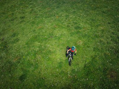 Dağ bisikleti süren bir kadının hava manzarası. Çiçekli çayırların tepesinde.