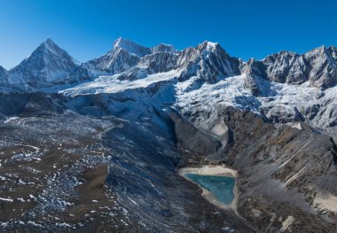 Açık mavi gökyüzüne karşı karla kaplı bir dağın çarpıcı fotoğrafı..