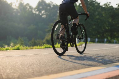 Mavi formalı bisikletçinin kırpılmış görüntüsü dağlardaki bir ormanın içinden geçen virajlı bir yolda bisiklet sürüyor. 