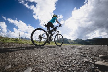 Mavi formalı bir kadın bisikletçi dağlardaki bir ormanın içinden bisikletini sürüyor. 