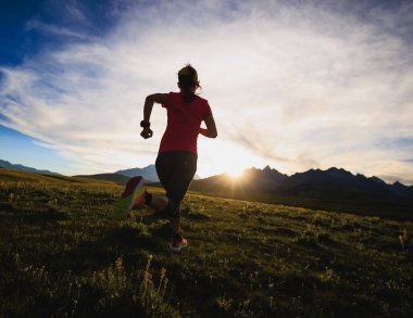 Kadın gün batımında yüksek irtifada çayırlarda koşuyor. 