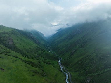 Puslu dağların arasından akan yemyeşil bir vadinin havadan görünüşü..