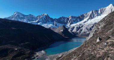 Turkuaz bir alp gölünün göz kamaştırıcı yüksek açılı manzarası bir vadide, pürüzsüz, karla kaplı dağlarla çevrili berrak mavi bir gökyüzünün altında..