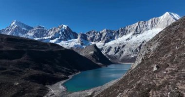 Turkuaz bir alp gölünün göz kamaştırıcı yüksek açılı manzarası bir vadide, pürüzsüz, karla kaplı dağlarla çevrili berrak mavi bir gökyüzünün altında..