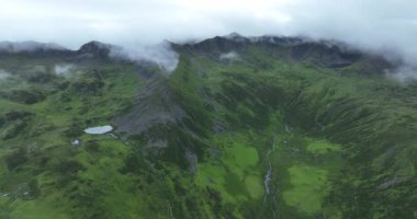 Uçsuz bucaksız, yemyeşil bir manzaranın yuvarlanan tepeleri kısmen alçak bulutlarla ya da bulutlu bir gökyüzünün altındaki sisle kaplı bir görüntüsü..