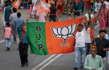 Bharatiya Janata Partisi (BJP) destekçileri, 29 Nisan 2024 'te Hindistan' ın Assam kentindeki Guwahati kentinde, Genel seçimlerin üçüncü safhası öncesinde, Birlik İçişleri Bakanı Amit Şah 'ın bir yol gösterisini izlemek üzere geldiklerinde bir BJP bayrağı tutuyorlar.. 