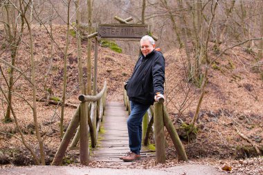 Ormandaki tahta köprüde kıdemli bir adam duruyor.