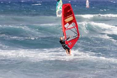 Tenerife-İspanya-Temmuz 2013: Kırmızı yelkenli rüzgar sörfü tahtasıyla okyanusta dalgıç kıyafetli genç bir adam. Tenerife, Kanarya Adaları, İspanya