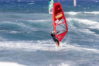 Tenerife-İspanya-Temmuz 2013: Kırmızı yelkenli rüzgar sörfü tahtasıyla okyanusta dalgıç kıyafetli genç bir adam. Tenerife, Kanarya Adaları, İspanya